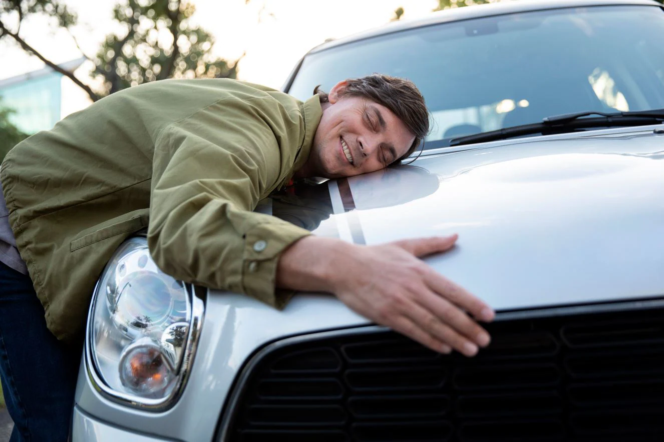 Person embracing a car, symbolizing 'no worries' and satisfaction